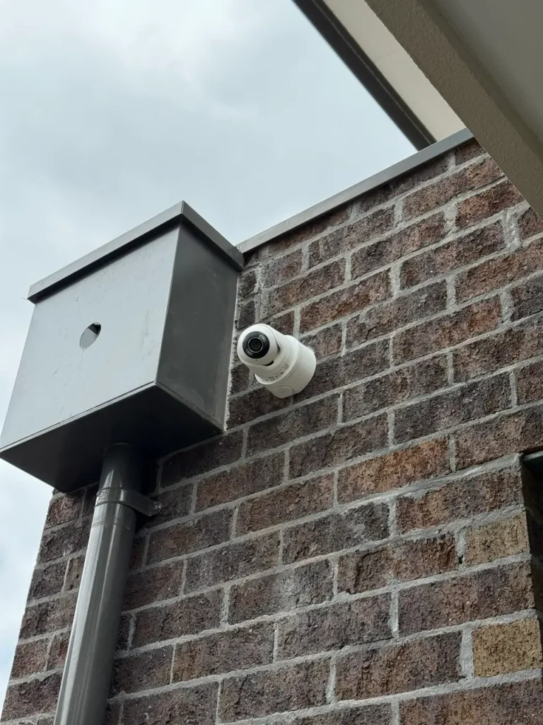 Bullet CCTV camera mounted on brick exterior wall beside electrical enclosure at a Melbourne property