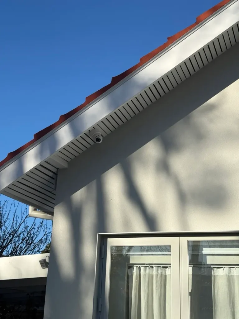 Dome CCTV camera installed under roofline eave of a white rendered home in Armadale covering rear yard and door access