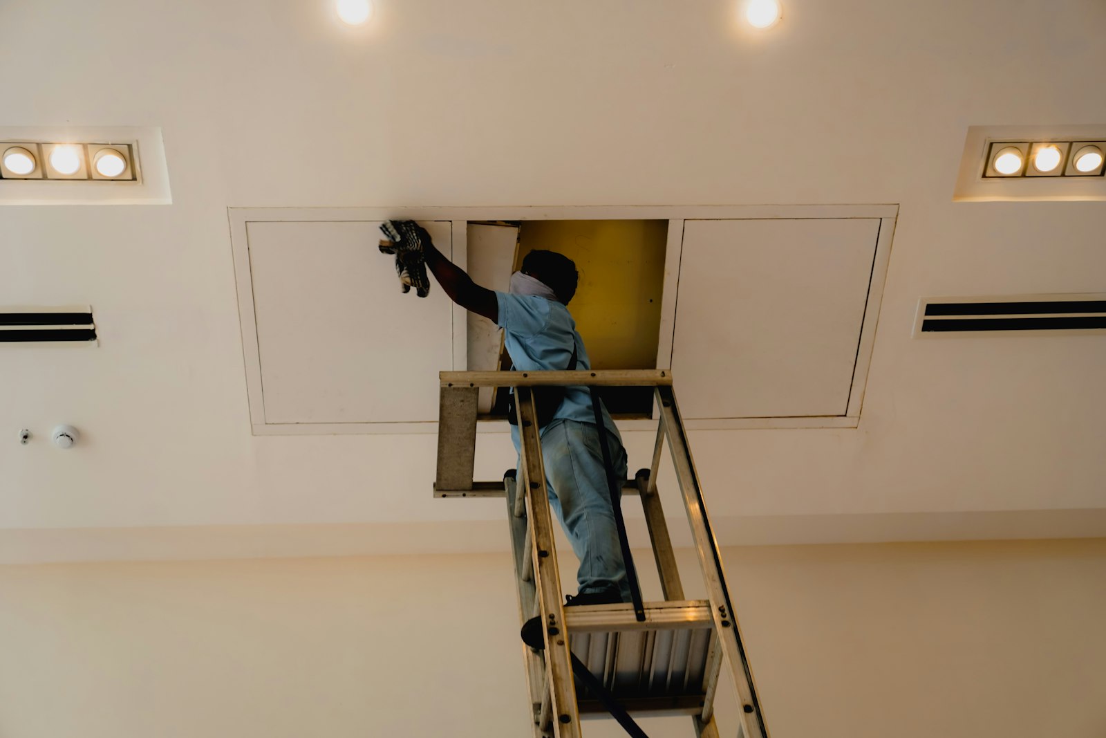 commercial-cctv-cost-melbourne-ceiling-cable-run - SIPKO Security Technician on a ladder working in a ceiling access panel while running cable for a commercial install
