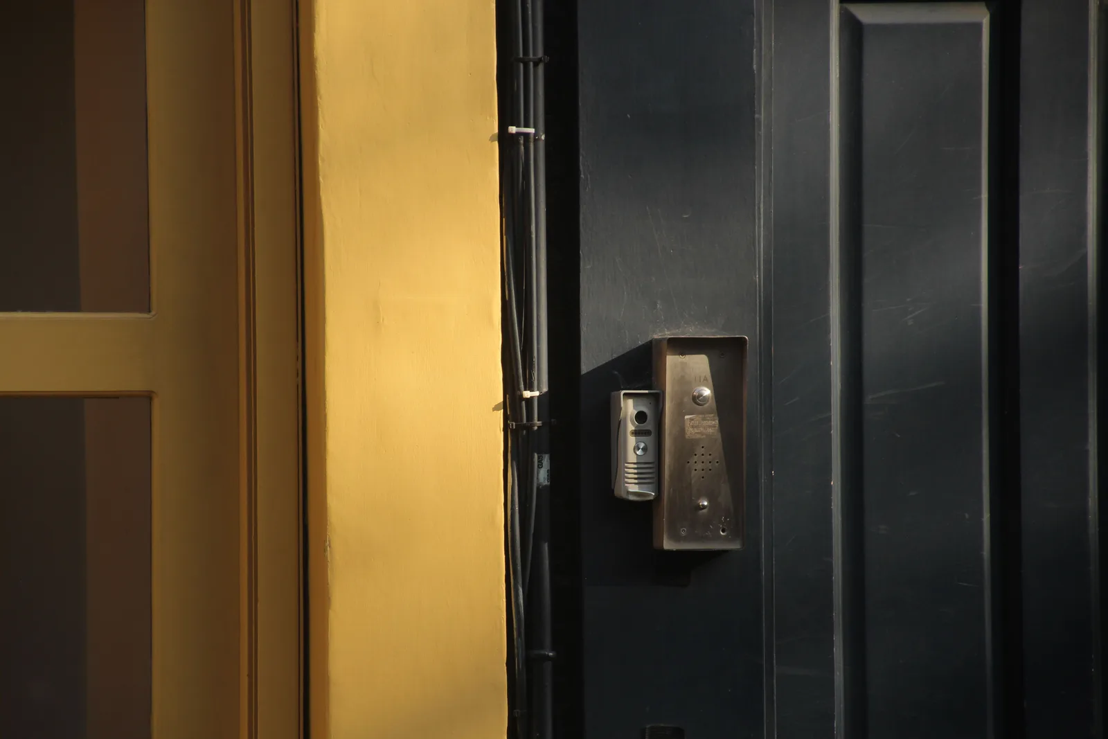 Metal intercom panels beside a dark entrance door and yellow door frame