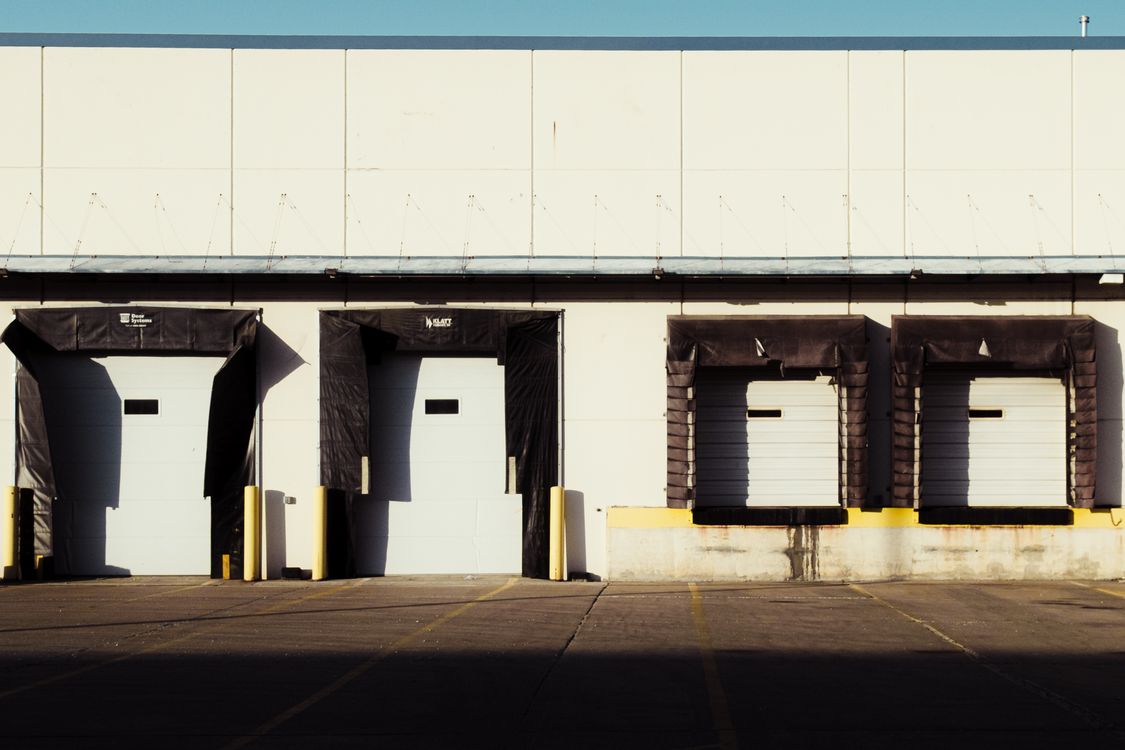 Warehouse loading bays and access area - SIPKO Security Four closed warehouse loading bays with yellow safety bollards and an empty paved loading area.