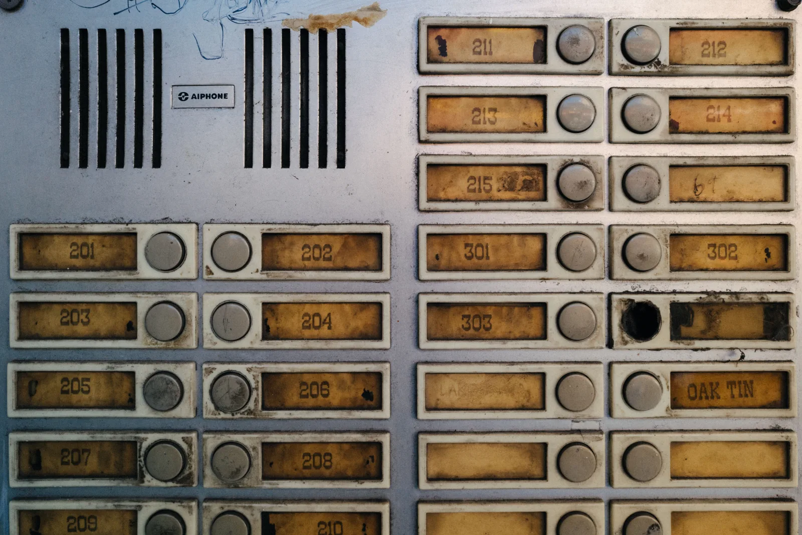 Older apartment intercom panel with numbered call buttons and a speaker grille