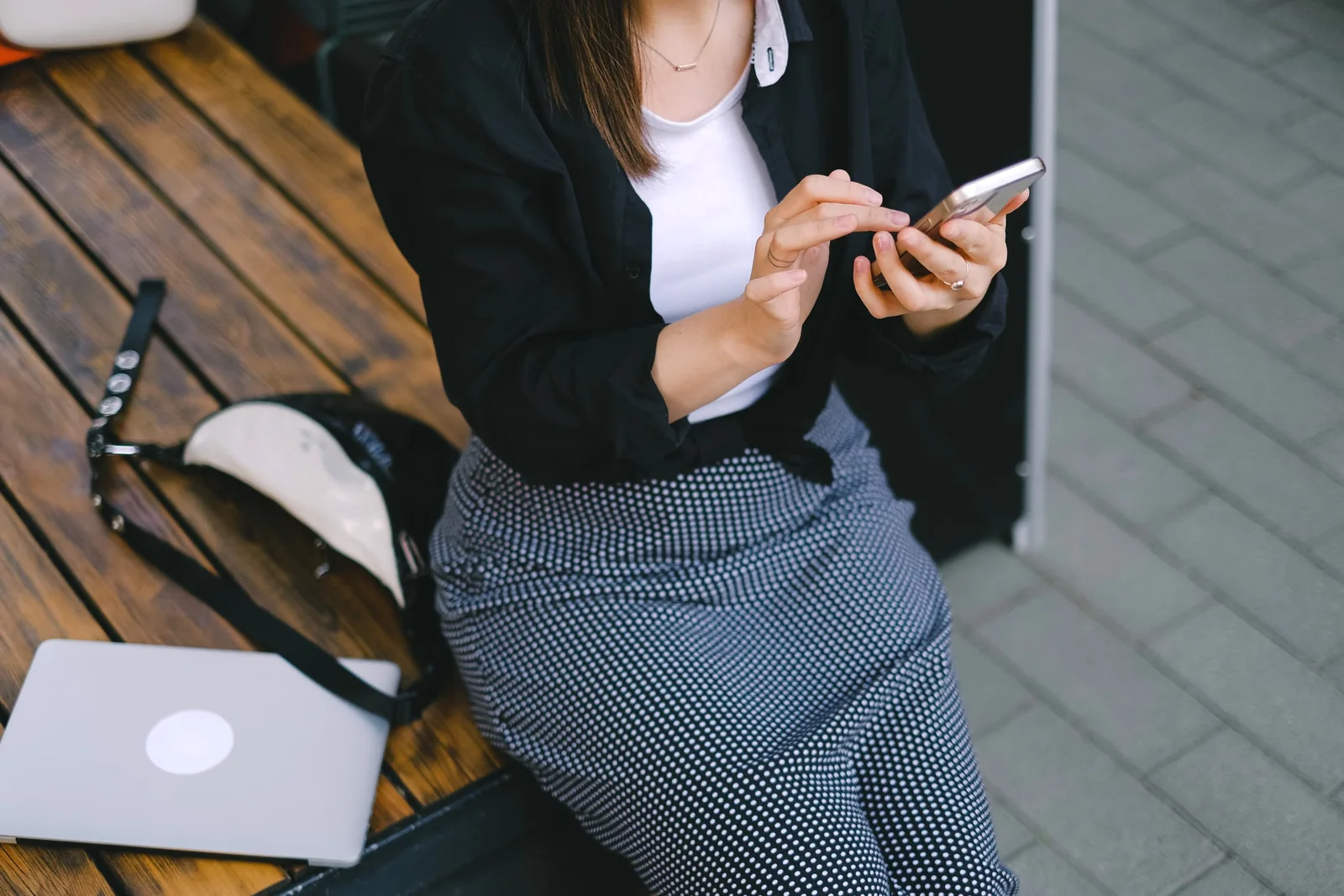 Smartphone use outdoors - SIPKO Security Woman using a smartphone while seated on an outdoor wooden bench.