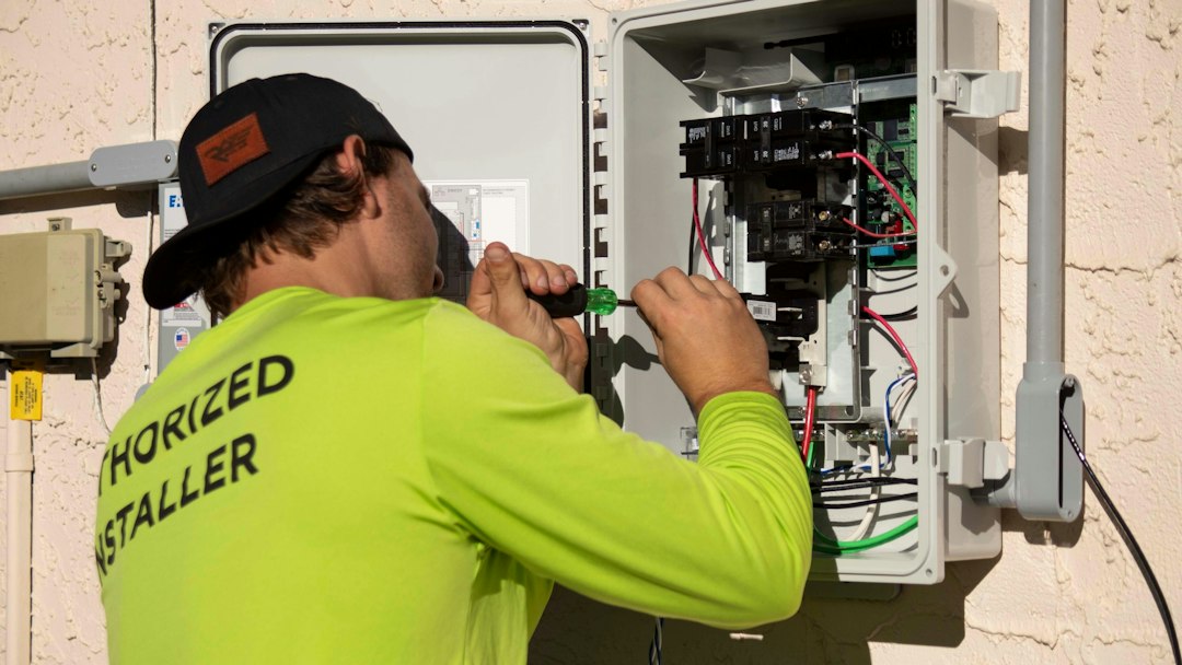 ajax-alarm-vs-risco-alarm-panel-install - SIPKO Security A technician in a high-visibility shirt working on a wall-mounted electrical panel