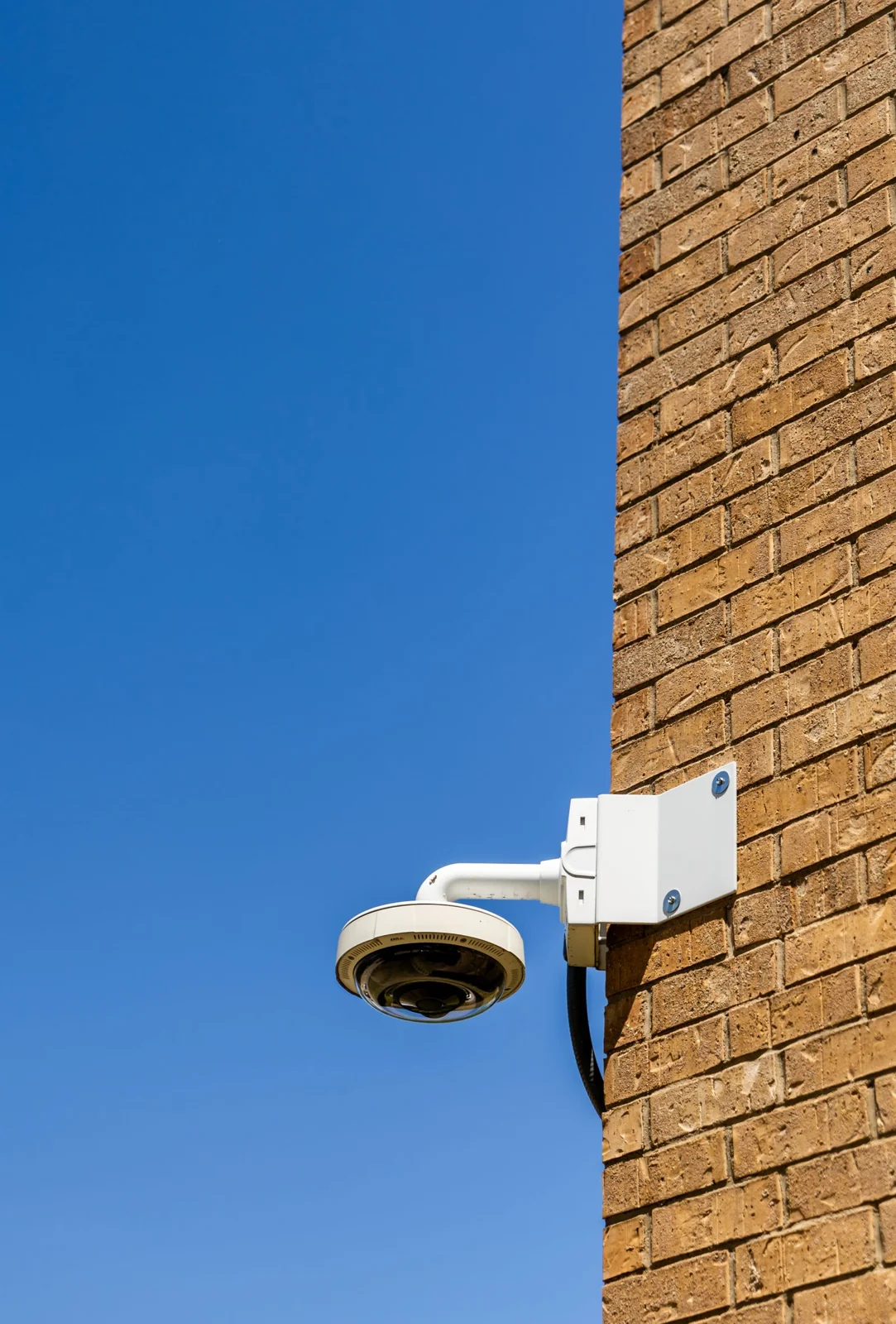 Outdoor security camera on a brick wall against blue sky