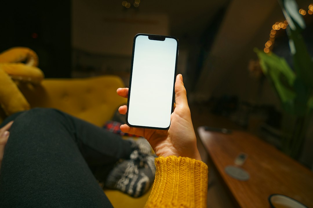 lower security alarm cost - self-monitoring phone - SIPKO Security Person sitting on a couch holding a smartphone
