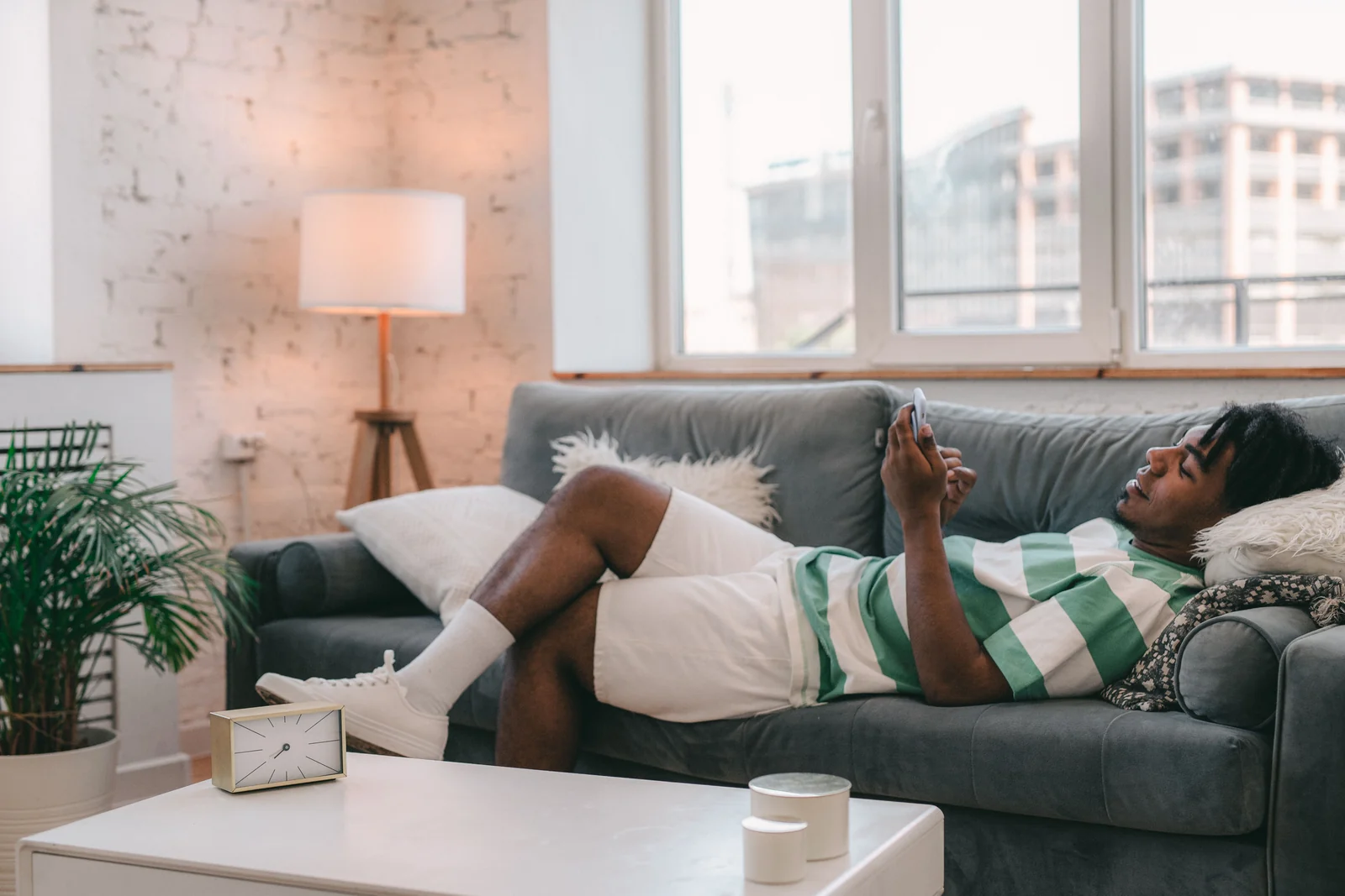 Man checking phone on sofa - SIPKO Security Man using a smartphone while relaxing on a grey sofa at home