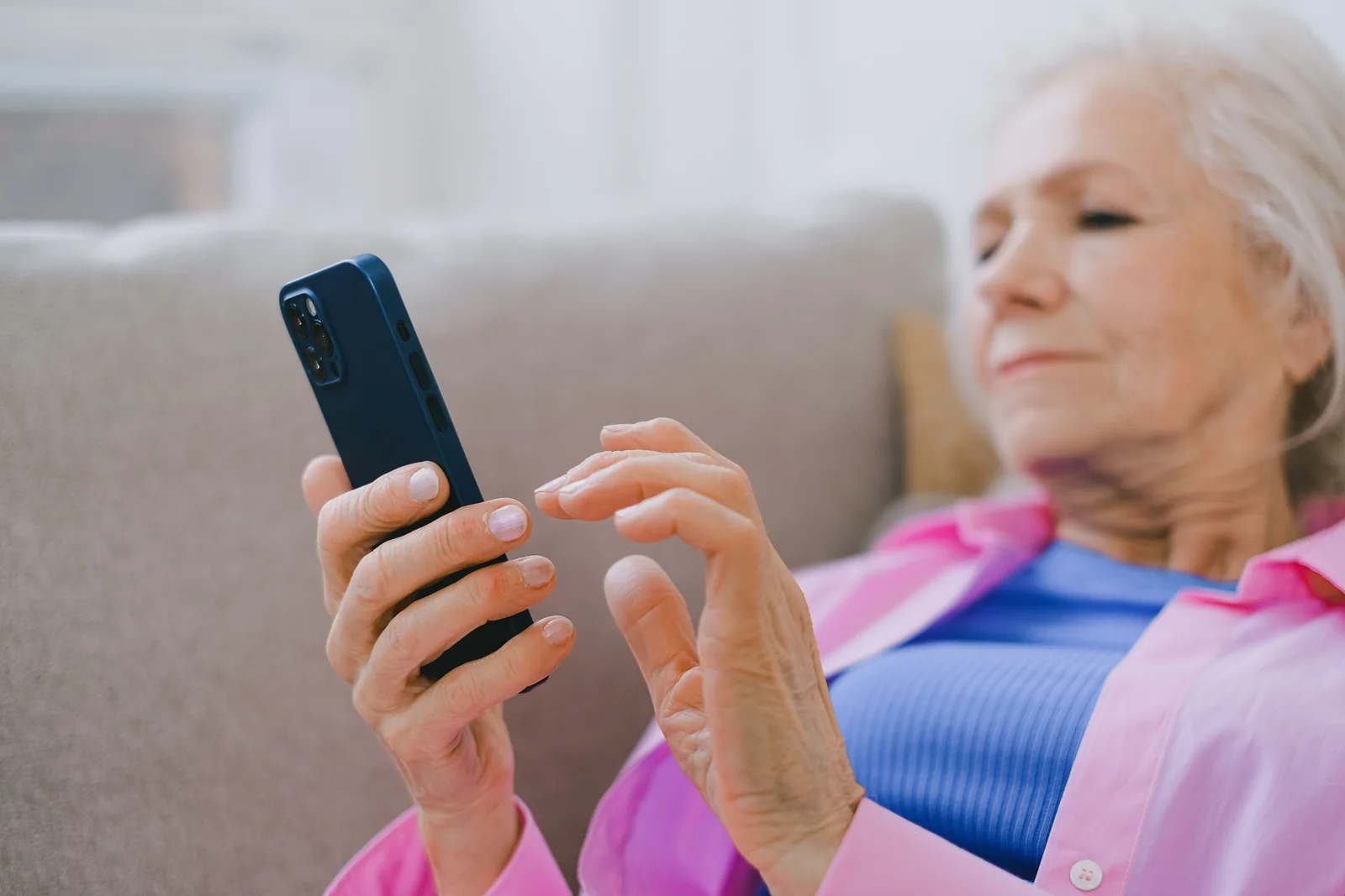 Older woman using a smartphone at home - SIPKO Security Older woman in a pink shirt using a smartphone on a sofa at home