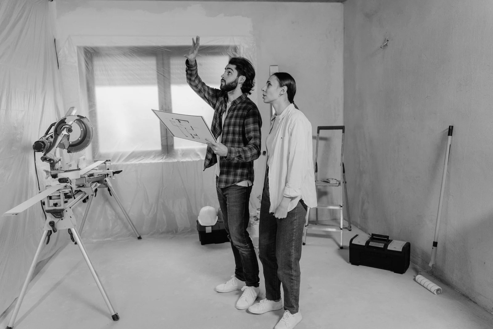 Two people reviewing a floor plan inside a room being renovated